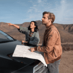 Two travellers planning a route with a paper map on the bonnet of a car in the Kazakh hills