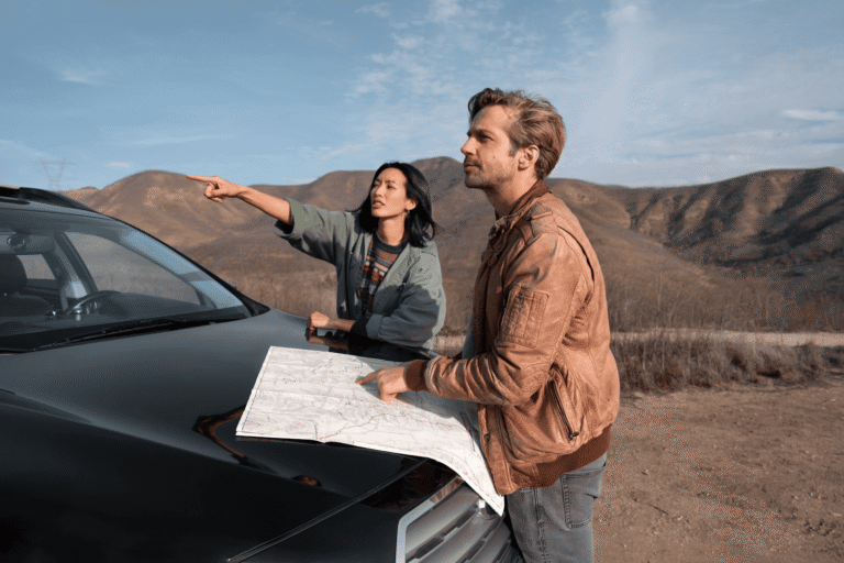Two travellers planning a route with a paper map on the bonnet of a car in the Kazakh hills